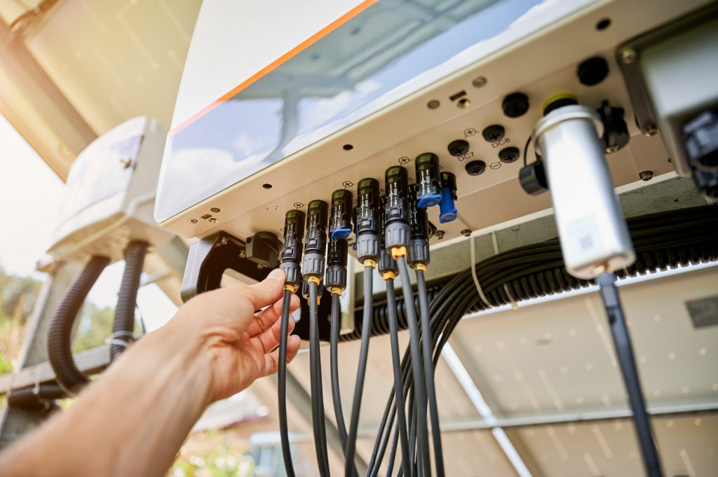 Während der Installation oder Wartung verbindet die Hand einer Person schwarze Kabel mit Anschlüssen unter einem Solarpanel-Steuerkasten.
