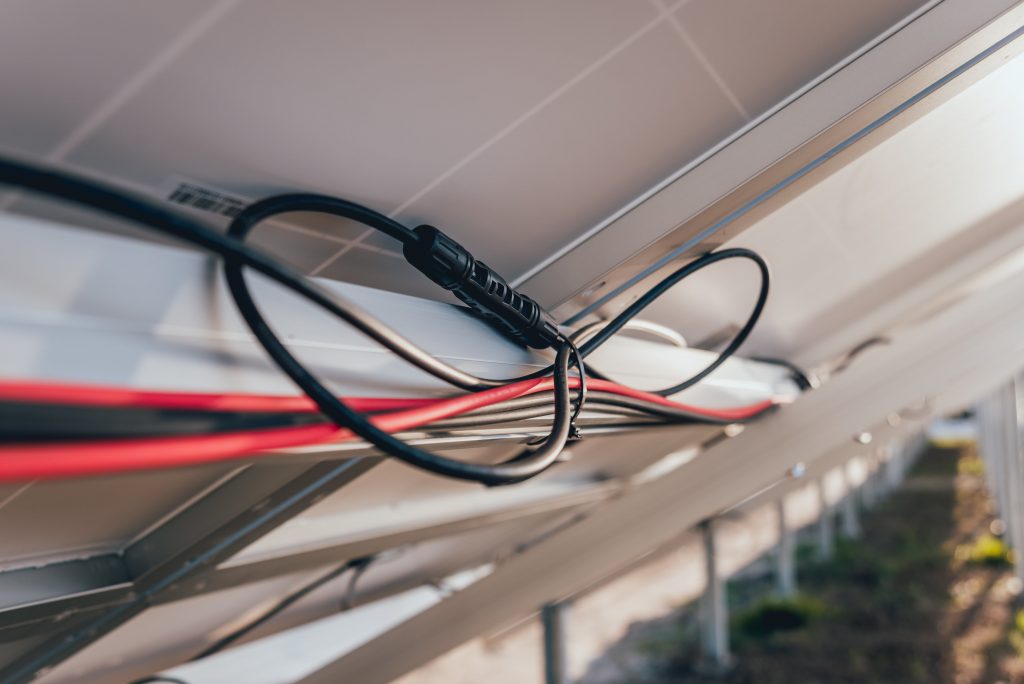 Nahaufnahme von elektrischen Kabeln und Anschlüssen, die an der Unterseite einer Solarpanelanlage angebracht sind.